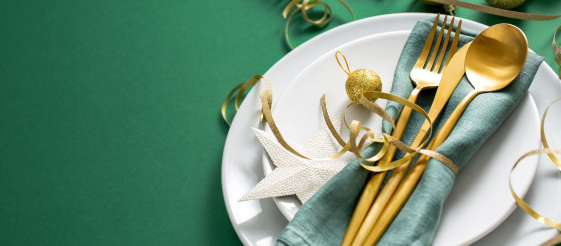Christmas Flat Lay Background. Gold Cutlery with Bubbles served on napkin on plate on Green Background. Minimalistic design. Copy Space. Horizontal. Christmas concept.